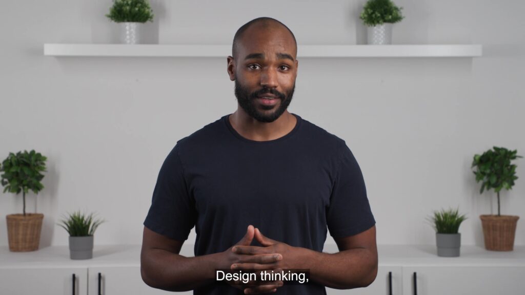 An instructor standing tall in a confident manner against a white backdrop with plants. 