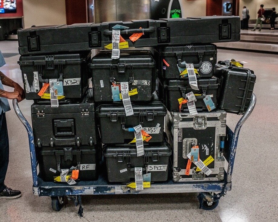 Video production equipment securely packed in hard cases, placed on an airport trolley, ready for international shipping.